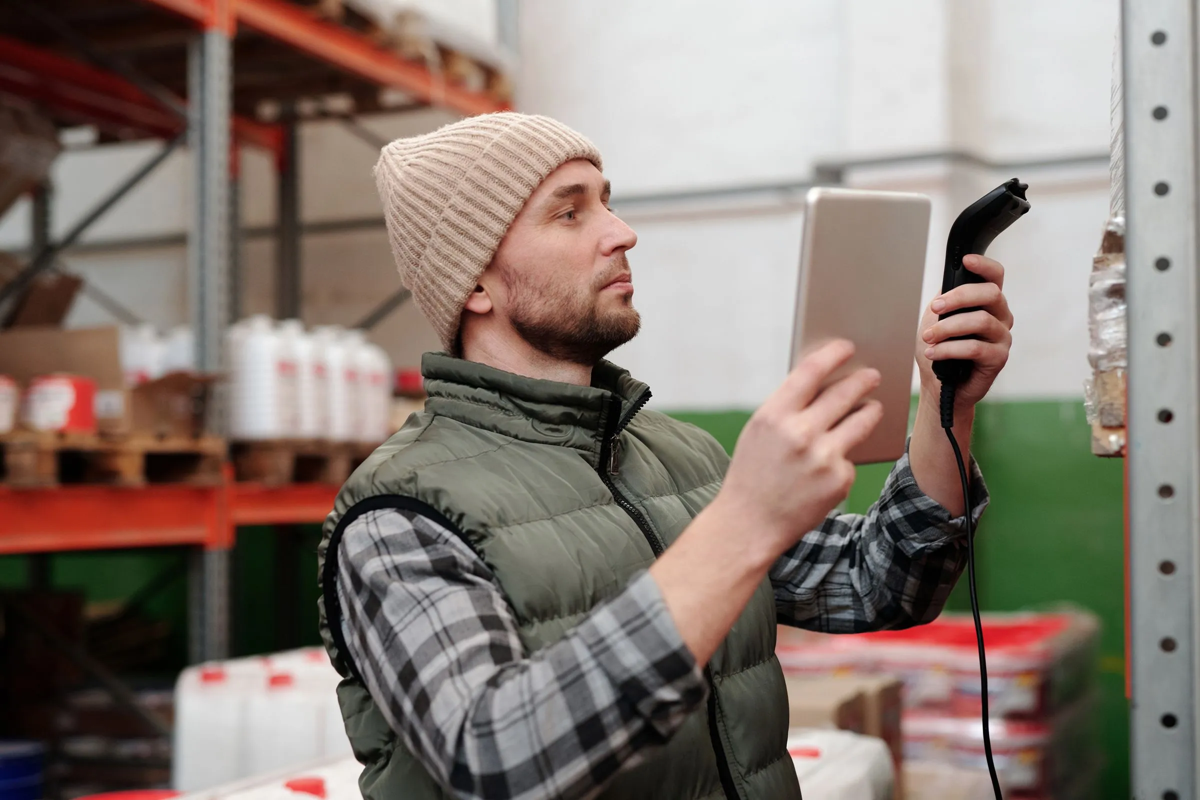 Warehouse worker scanning inventory with a handheld scanner and tablet between storage racks